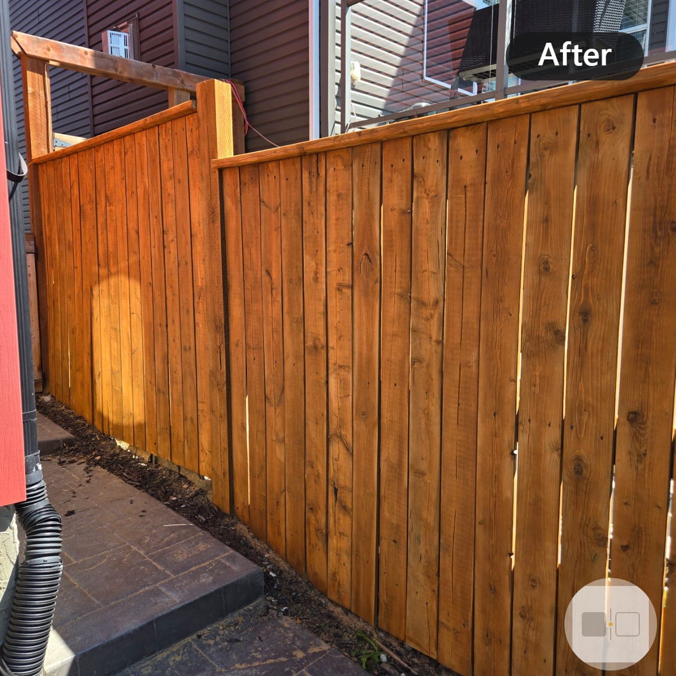 The same cedar fence after staining, rich warm orange-brown finish