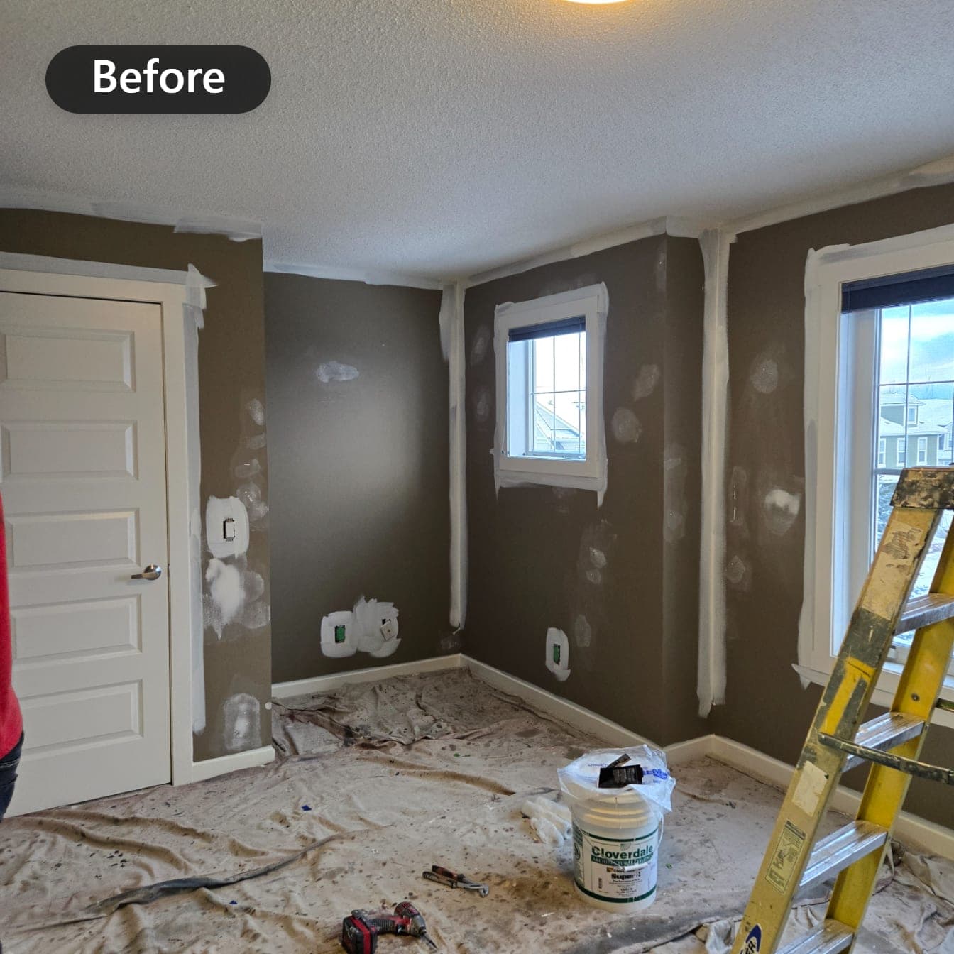 Bedroom with dark brown walls during preparation, filled patches, masked trim and drop cloths over the carpet